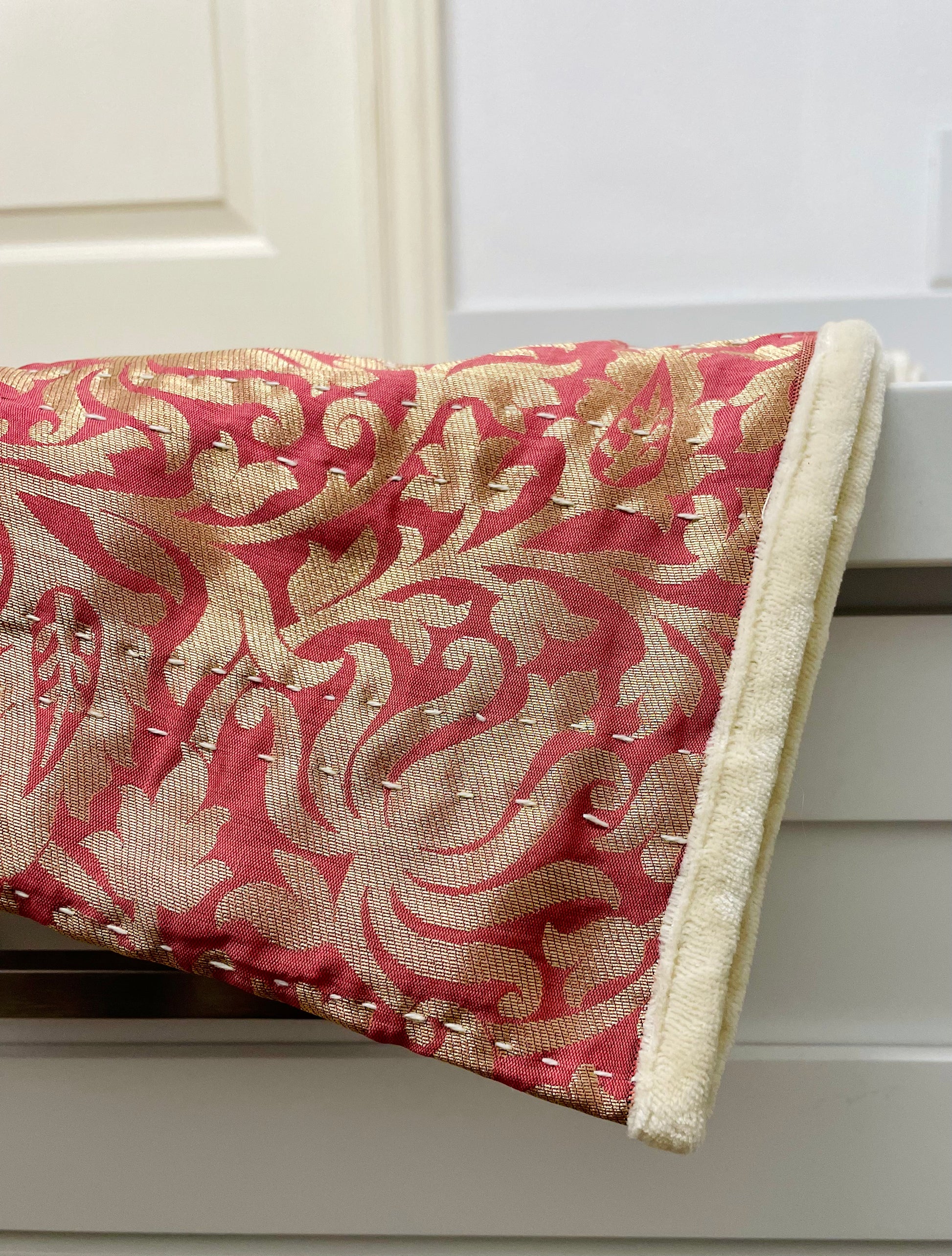 Red and beige patterned fabric with decorative stitching on a wooden surface.